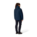 A person with curly hair in a ponytail stands facing away from the camera against a white background, wearing the Rab Womens Microlight Shield Waterproof Down Jacket in dark blue, paired with dark pants and black shoes.