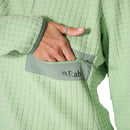 A person wearing a light green Rab Womens Ramshaw Pull-On Fleece with a textured grid pattern opens a zippered chest pocket with their right hand. Only their torso and hand are visible.
