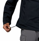 Person wearing a black Columbia waterproof jacket with a white background while they adjust the hem using a drawstring