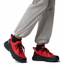 Red and black hiking boots worn with light gray pants on a white background