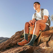 Man sitting on a rocky mountain top wearing hiking shoes and socks.
