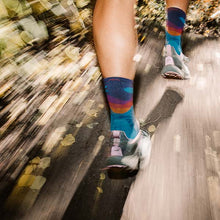 Person running on a trail wearing colorful Darn Tough running socks and running shoes.