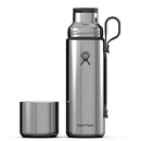 A Hydro Flask 28 oz (828 ml) Hot Flask & Cup, made of stainless steel and equipped with a black lid and handle, stands upright alongside its matching metal cup on a white background. Featuring advanced vacuum insulation, this flask keeps beverages hot or cold for hours.