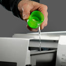 Hand pouring green liquid from a bottle into a machine on a gray background