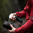 Person in red jacket using the grangers odour eliminator spray bottle on a black shoe outdoors