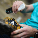 Person applying grangers odour eliminator to a black and yellow shoe with a blurred background