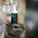 Spray bottle labeled 'Grangers Rubber Boot Care' on a stone surface with a natural background.