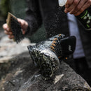 Person applying a white powdery substance to a black boot on a rock surface.
