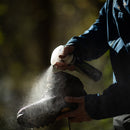 Person applying a white powdery substance to a black boot outdoors.
