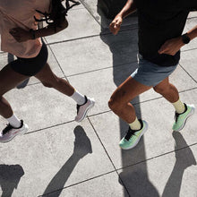 Two people running on a paved surface, focusing on their lower bodies and shoes.