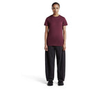 A person wearing a maroon Women’s 150 Tech Lite T-Shirt, dark grey wide-leg trousers, and black sneakers.