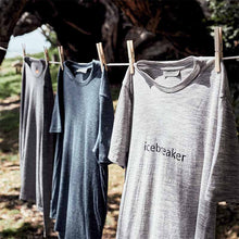 Three Icebreaker technical t-shirts in gray and blue tones hanging on a clothesline outdoors under a tree, with the front shirt reading 'icebreaker'.