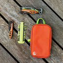 A multitool, folding knife, bit driver kit, and an orange Leatherman® Tool Pouch by Leatherman—crafted from rPET ripstop nylon with weather-resistant zippers—are arranged on a wooden surface.