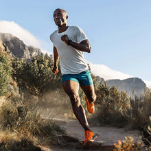 Man running on a trail with mountains in the background using HOKA trail running shoes