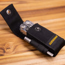 Leatherman nylon sheath with a tool sharpener in the pocket and a stainless steel multitool in the pouch on a wooden surface