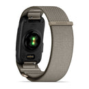 A close-up of the back of the Garmin CIRQA Smart Band with a fabric strap, displaying green sensor lights and charging contacts—emphasizing its 24/7 health monitoring features for advanced wellness insights.