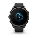 A Garmin fēnix 9 multisport GPS smartwatch in black shows a blue glowing triangle with a microphone and phone icon at its center, suggesting voice or phone capabilities.