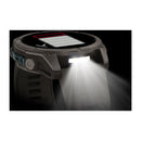 The Garmin fēnix 9, a rugged multisport GPS smartwatch, shines a bright white flashlight from its side to cut through the darkness. Its AMOLED display is partially visible, displaying a status or battery bar.