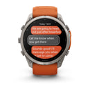 The Garmin fēnix 9 Pro inReach multisport GPS smartwatch with an orange band shows a text message conversation about heading out after breakfast and messaging upon arrival at camp.