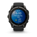 A Garmin fēnix 9 multisport GPS smartwatch in black features a vibrant round AMOLED display showing the time as 6:00, a sunny weather icon, a temperature of 23°C, the date as Saturday the 1st, and the greeting “Good Morning, Alex!”.