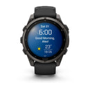 A Garmin fēnix 9 multisport GPS smartwatch in black features a vibrant round AMOLED display showing the time (6:00), date (Sat 01), greeting (“Good Morning, Alex!”), and weather (23°C, 18/26, sunny), complemented by a sleek black band.