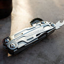 A Leatherman Rev Multitool rests on a sunlit surface, partially open to display its locking blade and bottle opener, with the Leatherman branding engraved on the side.