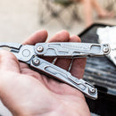 A hand holds an open Leatherman Rev Multitool with locking blade and pliers near a grill in an outdoor setting.