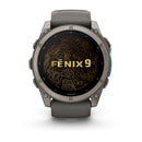 A Garmin fēnix 9 multisport GPS smartwatch in gray showcases the text “FENIX 9” on its vivid AMOLED display, featuring a gold topographic map design in the background.