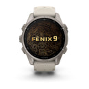 A Garmin fēnix 9 multisport GPS smartwatch with a beige band shows “fēnix 9” on its AMOLED display over a black and gold topographic map design.