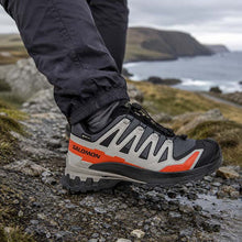 Person wearing Salomon hiking shoes on a rocky trail with ocean and cliffs in the background