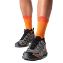 Person wearing orange socks and black and gray Salomon XA PRO shoes on a white background