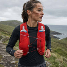 Woman wearing a red Salomon running vest in a scenic outdoor setting.