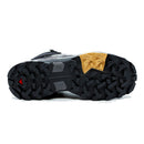 The image shows the sole of a Salomon Womens X-Ultra 5 Mid GORE-TEX Hiking Boot, featuring rugged black multidirectional treads, a yellow geometric section by the heel, and a red triangle near the toe, highlighting its advanced waterproof design.