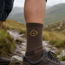 Brown sock with a yellow logo worn by a person on a mountain trail