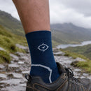 Person wearing a blue sock with a logo, standing on a mountain path with a scenic view.