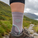 Person wearing a gray sock with a green logo on a mountain trail