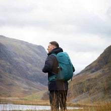 Person with a teal backpack standing in a mountainous landscape