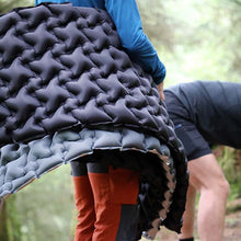 Person holding a large quilted sleeping pad outdoors