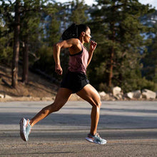 Woman running on a road with trees in the background using HOKA running shoes.